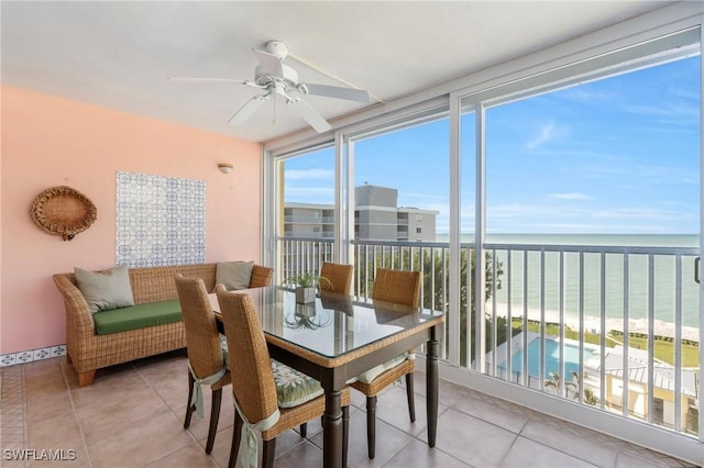 sunroom with ceiling fan, a view of the beach, and a water view