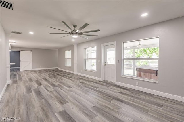 unfurnished living room with a barn door, light hardwood / wood-style floors, and ceiling fan