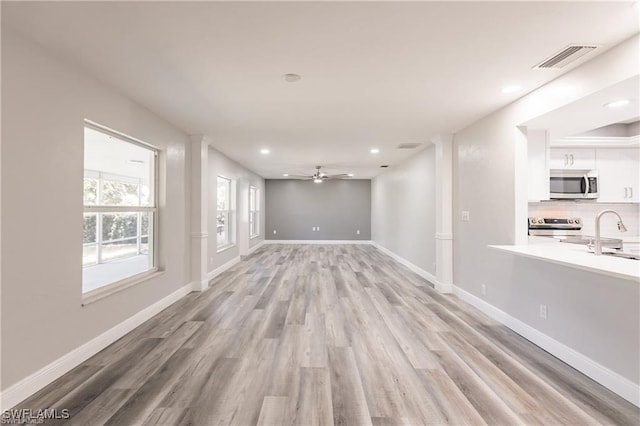 unfurnished living room with ceiling fan, sink, and light wood-type flooring