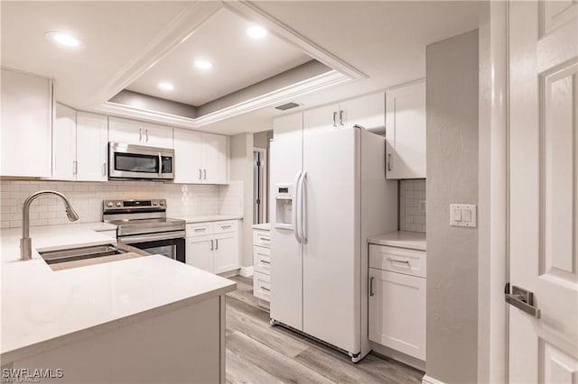 kitchen featuring appliances with stainless steel finishes, tasteful backsplash, a raised ceiling, sink, and white cabinetry