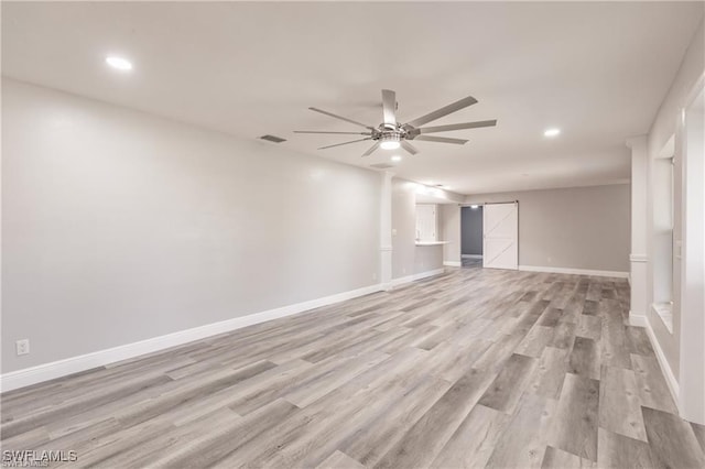 empty room featuring ceiling fan, light hardwood / wood-style floors, and a barn door