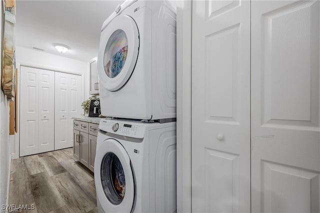 laundry room featuring stacked washer / dryer, cabinets, and light hardwood / wood-style floors