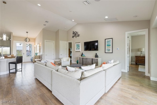 living room featuring light wood-type flooring, vaulted ceiling, and a notable chandelier