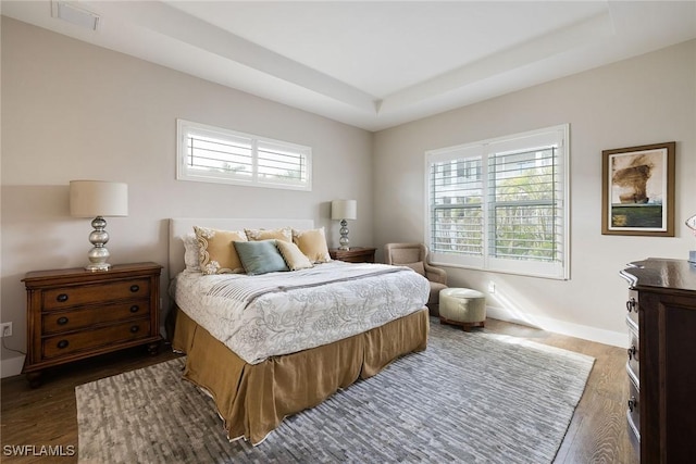 bedroom with a raised ceiling, dark wood-type flooring, and multiple windows