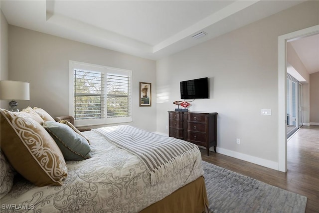 bedroom with dark hardwood / wood-style floors and a raised ceiling