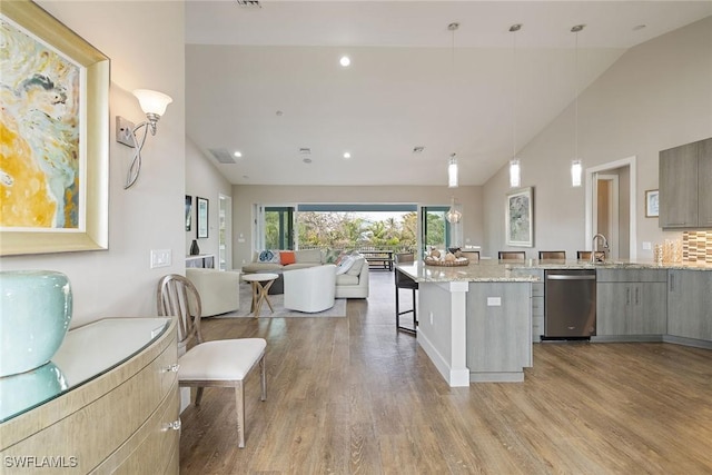 kitchen featuring dishwasher, hanging light fixtures, light stone counters, light hardwood / wood-style flooring, and a kitchen bar