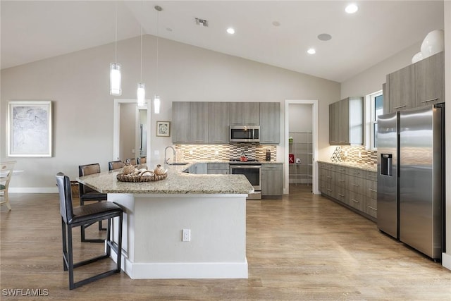 kitchen with a kitchen bar, light stone countertops, tasteful backsplash, stainless steel appliances, and sink