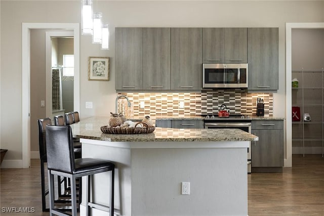 kitchen with light stone countertops, hanging light fixtures, stainless steel appliances, a kitchen bar, and decorative backsplash