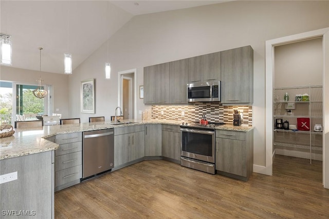 kitchen featuring hardwood / wood-style floors, hanging light fixtures, decorative backsplash, light stone countertops, and stainless steel appliances