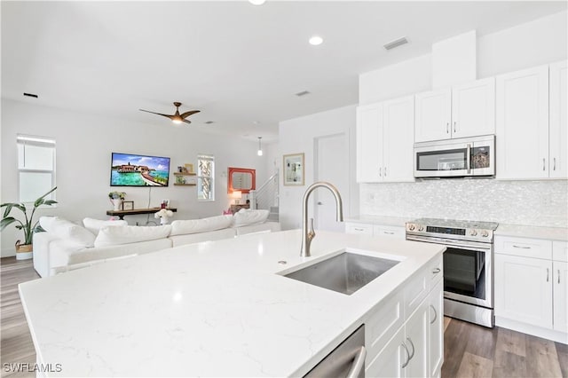 kitchen with light stone counters, a center island with sink, tasteful backsplash, appliances with stainless steel finishes, and sink