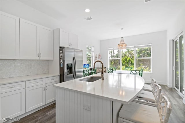 kitchen with a kitchen island with sink, pendant lighting, stainless steel refrigerator with ice dispenser, sink, and white cabinetry