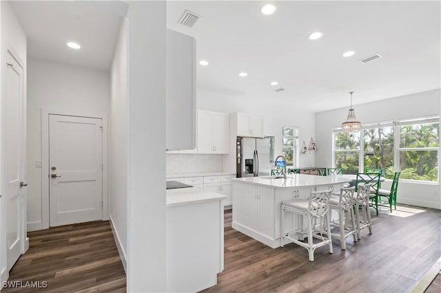 kitchen featuring white cabinetry, a kitchen island with sink, hanging light fixtures, stainless steel refrigerator with ice dispenser, and a breakfast bar