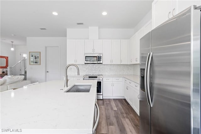 kitchen with light stone counters, tasteful backsplash, white cabinets, appliances with stainless steel finishes, and sink