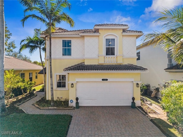 mediterranean / spanish home with decorative driveway, a tiled roof, an attached garage, and stucco siding