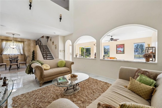 living room with arched walkways, marble finish floor, ceiling fan, baseboards, and stairs