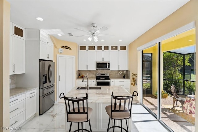 kitchen with appliances with stainless steel finishes, a sink, light stone counters, and white cabinets