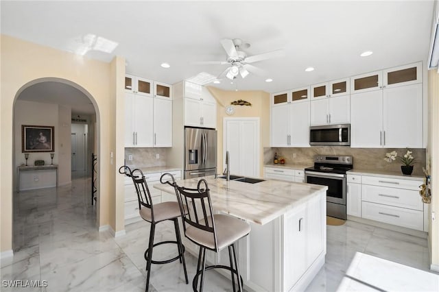 kitchen with marble finish floor, a center island with sink, stainless steel appliances, glass insert cabinets, and a sink