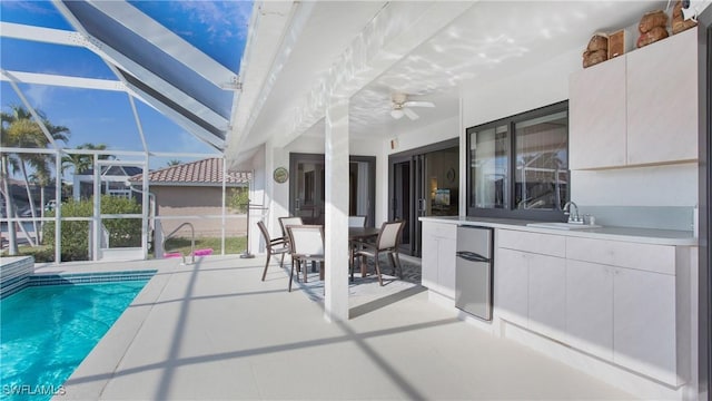 view of swimming pool featuring ceiling fan, a patio, glass enclosure, and an outdoor wet bar