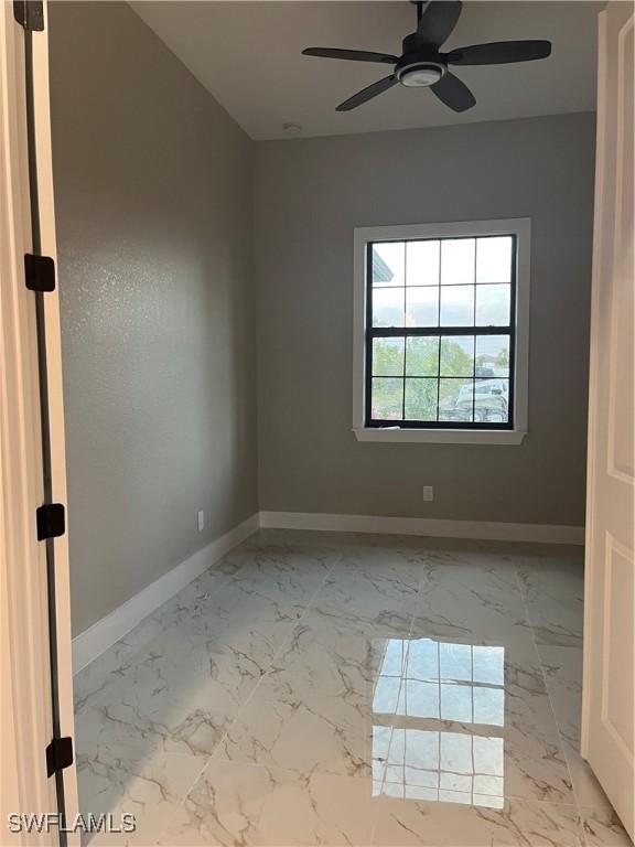 empty room featuring marble finish floor, a ceiling fan, and baseboards