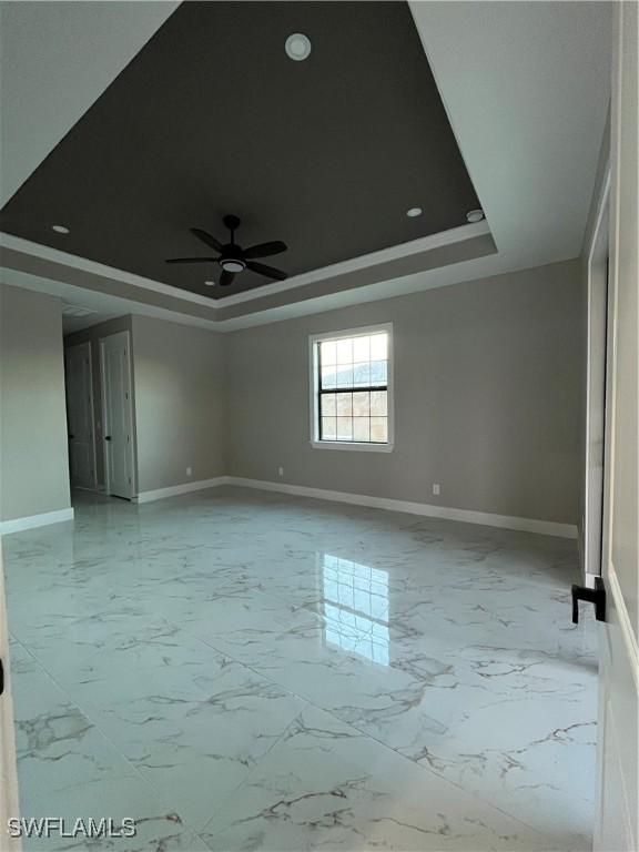 spare room with ceiling fan, baseboards, marble finish floor, and a tray ceiling