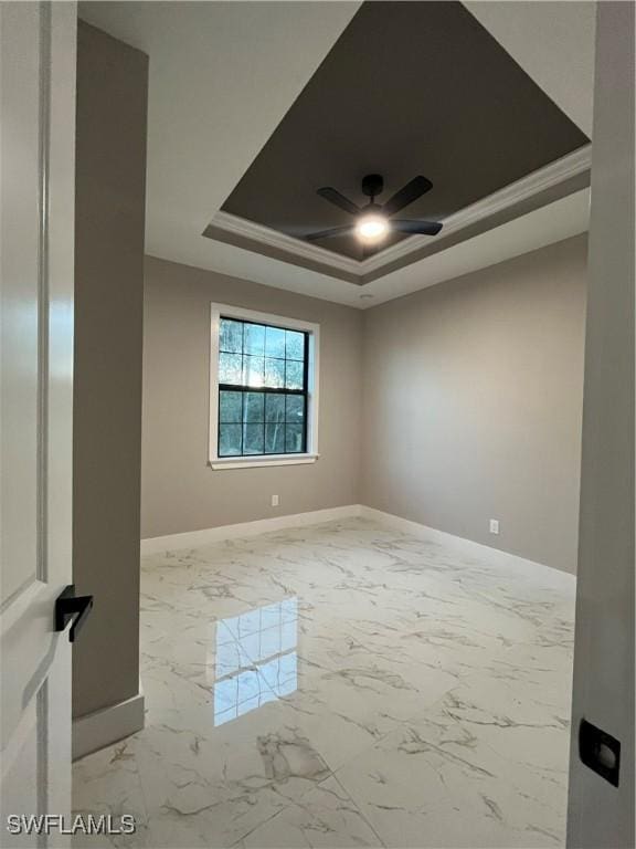 spare room with marble finish floor, baseboards, a ceiling fan, and a raised ceiling