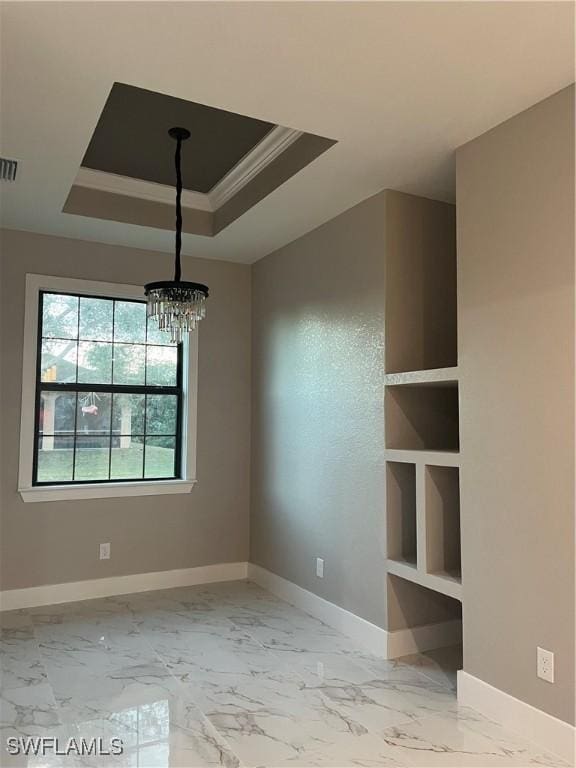 unfurnished dining area featuring built in shelves, a raised ceiling, ornamental molding, and a chandelier