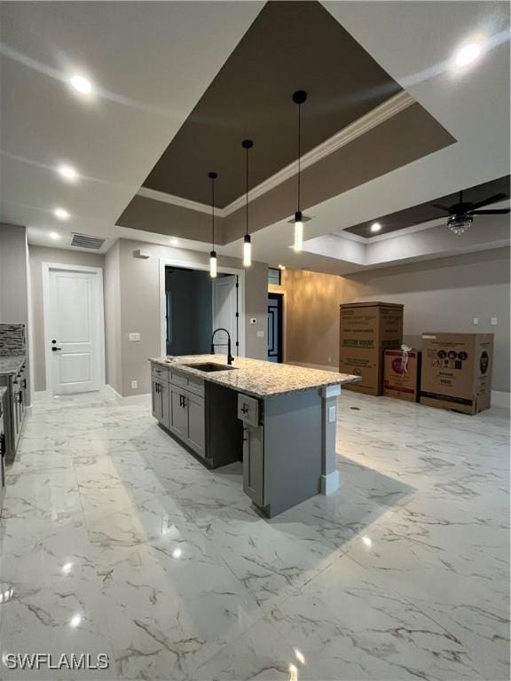 kitchen featuring sink, hanging light fixtures, a tray ceiling, a kitchen island with sink, and ornamental molding