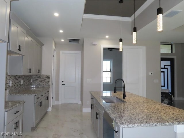 kitchen featuring decorative light fixtures, tasteful backsplash, sink, a kitchen island with sink, and light stone countertops