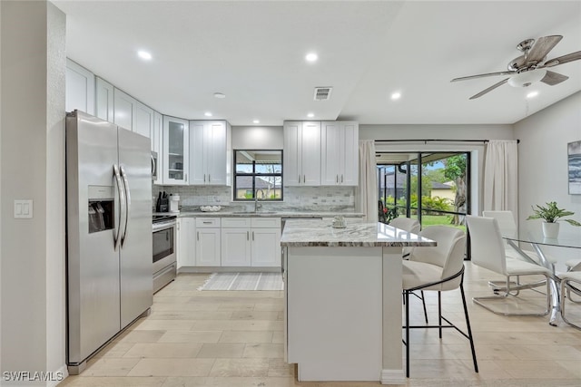 kitchen featuring appliances with stainless steel finishes, a breakfast bar, light stone counters, white cabinets, and sink