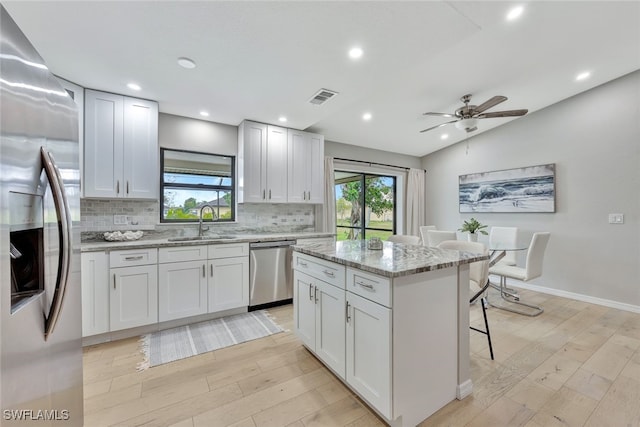 kitchen with vaulted ceiling, stainless steel appliances, light stone countertops, a kitchen island, and white cabinets