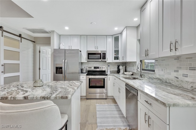 kitchen with a kitchen breakfast bar, a barn door, appliances with stainless steel finishes, sink, and white cabinetry