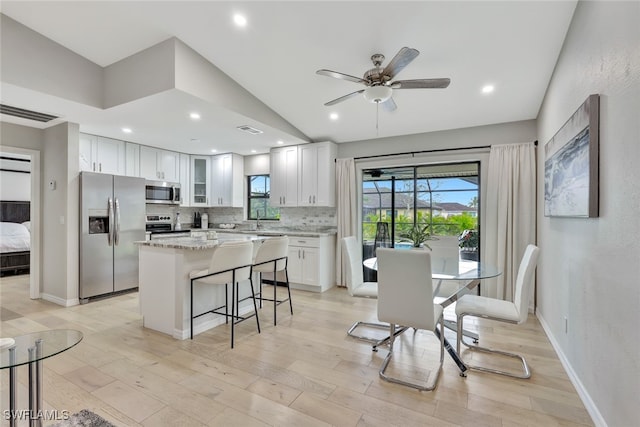 kitchen with appliances with stainless steel finishes, a center island, light stone countertops, decorative backsplash, and white cabinetry