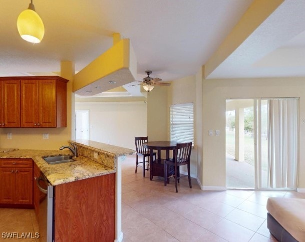 kitchen featuring pendant lighting, sink, ceiling fan, light stone counters, and kitchen peninsula