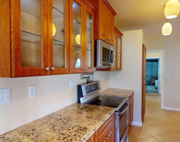 kitchen with light stone countertops, decorative light fixtures, stainless steel appliances, and light tile patterned floors