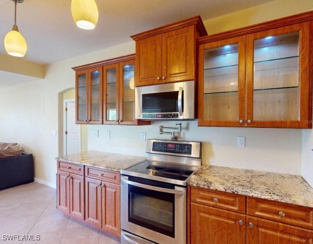 kitchen with pendant lighting, light stone counters, light tile patterned floors, and stainless steel appliances