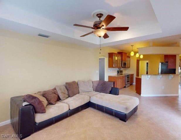 tiled living room featuring ceiling fan and a tray ceiling