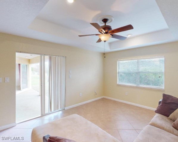 living room featuring light tile patterned floors, a raised ceiling, and ceiling fan