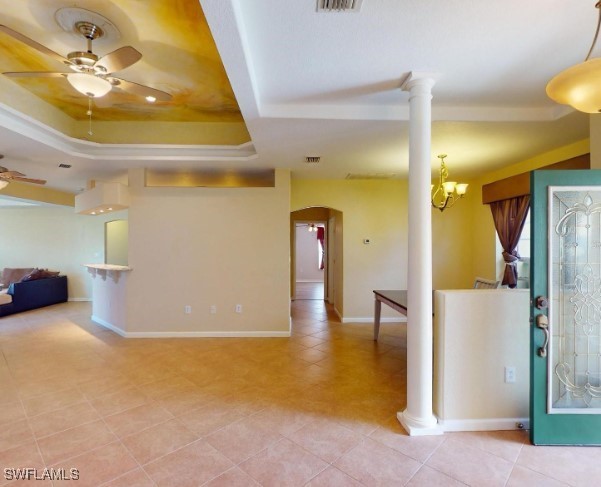 foyer entrance with light tile patterned floors, ceiling fan with notable chandelier, a raised ceiling, and ornate columns