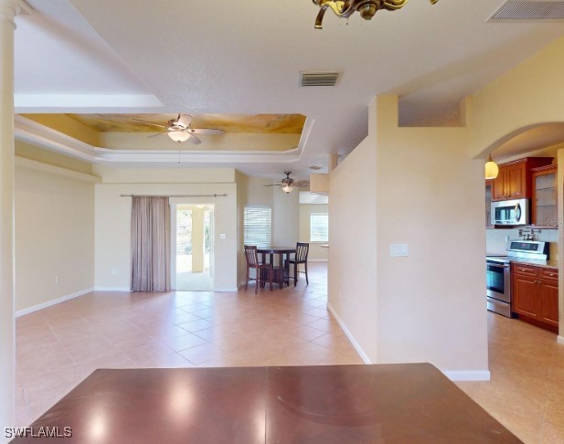 interior space featuring ceiling fan, a raised ceiling, light tile patterned floors, and appliances with stainless steel finishes