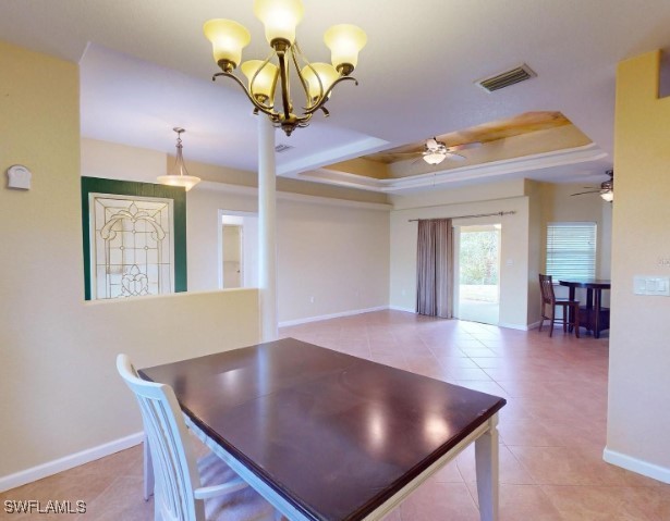 unfurnished dining area with light tile patterned floors, ceiling fan with notable chandelier, and a tray ceiling