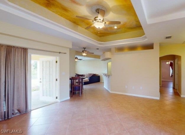 unfurnished room with ceiling fan, a raised ceiling, and light tile patterned floors