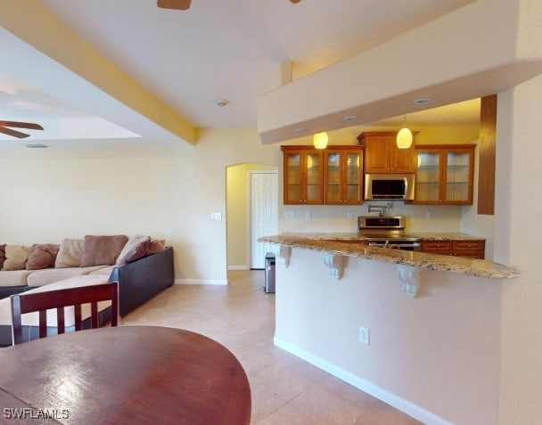 kitchen featuring light stone countertops, kitchen peninsula, decorative light fixtures, a breakfast bar area, and appliances with stainless steel finishes