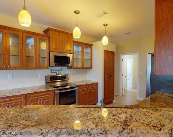 kitchen featuring light stone counters, light tile patterned floors, stainless steel appliances, and decorative light fixtures