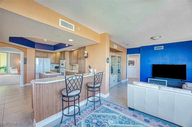 kitchen featuring white fridge, a breakfast bar area, light tile patterned floors, and kitchen peninsula