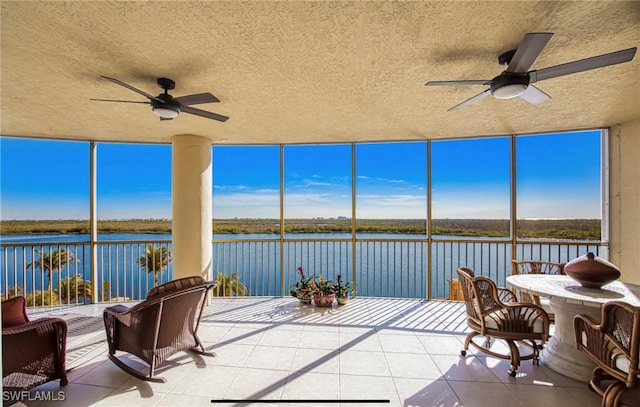 sunroom with ceiling fan and a water view