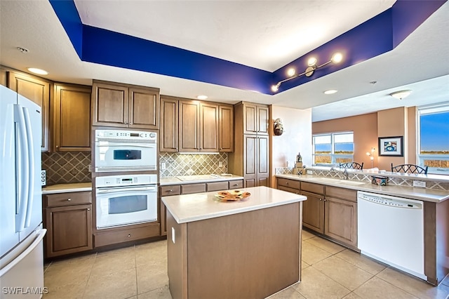 kitchen with sink, a center island, a tray ceiling, white appliances, and decorative backsplash