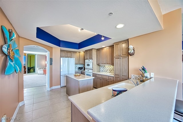 kitchen with tasteful backsplash, a center island, light tile patterned floors, a tray ceiling, and white appliances