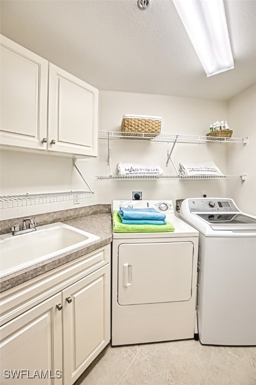 clothes washing area with sink, cabinets, light tile patterned floors, washing machine and dryer, and a textured ceiling