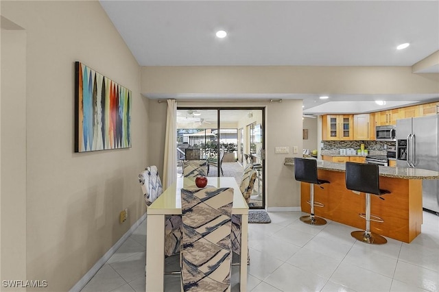 kitchen with a kitchen bar, decorative backsplash, kitchen peninsula, light stone counters, and stainless steel appliances