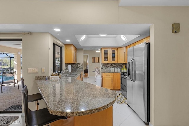 kitchen featuring kitchen peninsula, appliances with stainless steel finishes, a kitchen bar, decorative backsplash, and sink